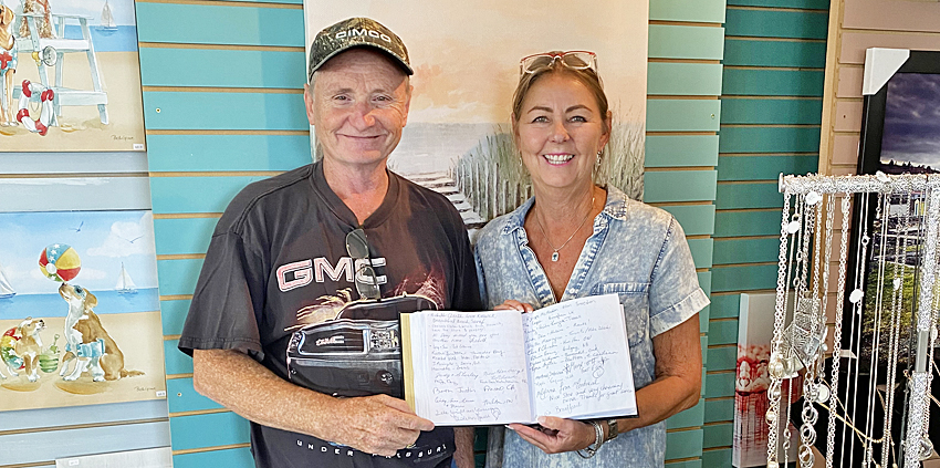 Man and woman smiling holding a guest book with pages of summer visitor names.